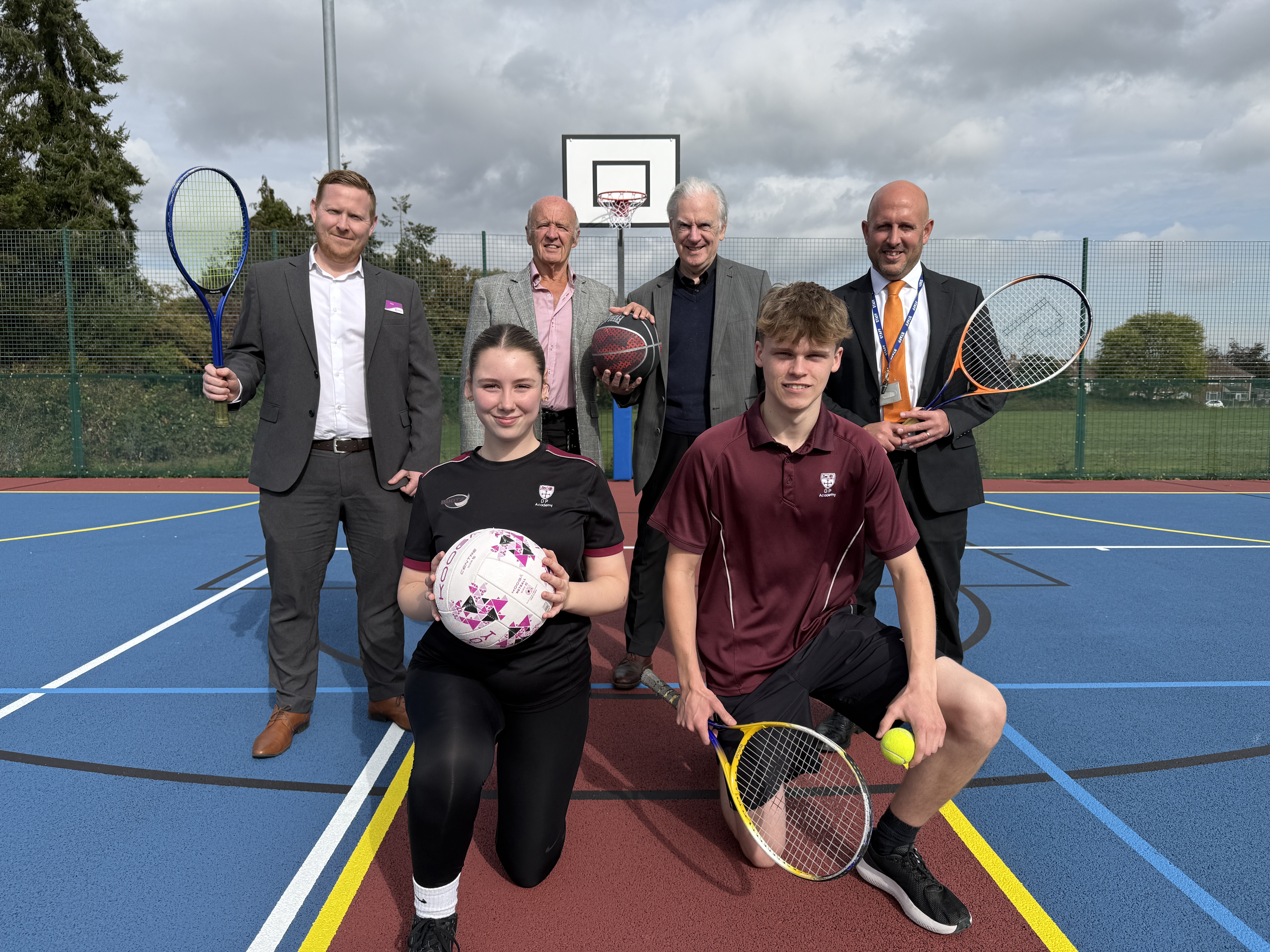 A group of people at an outdoor sports court holding tennis rackets.