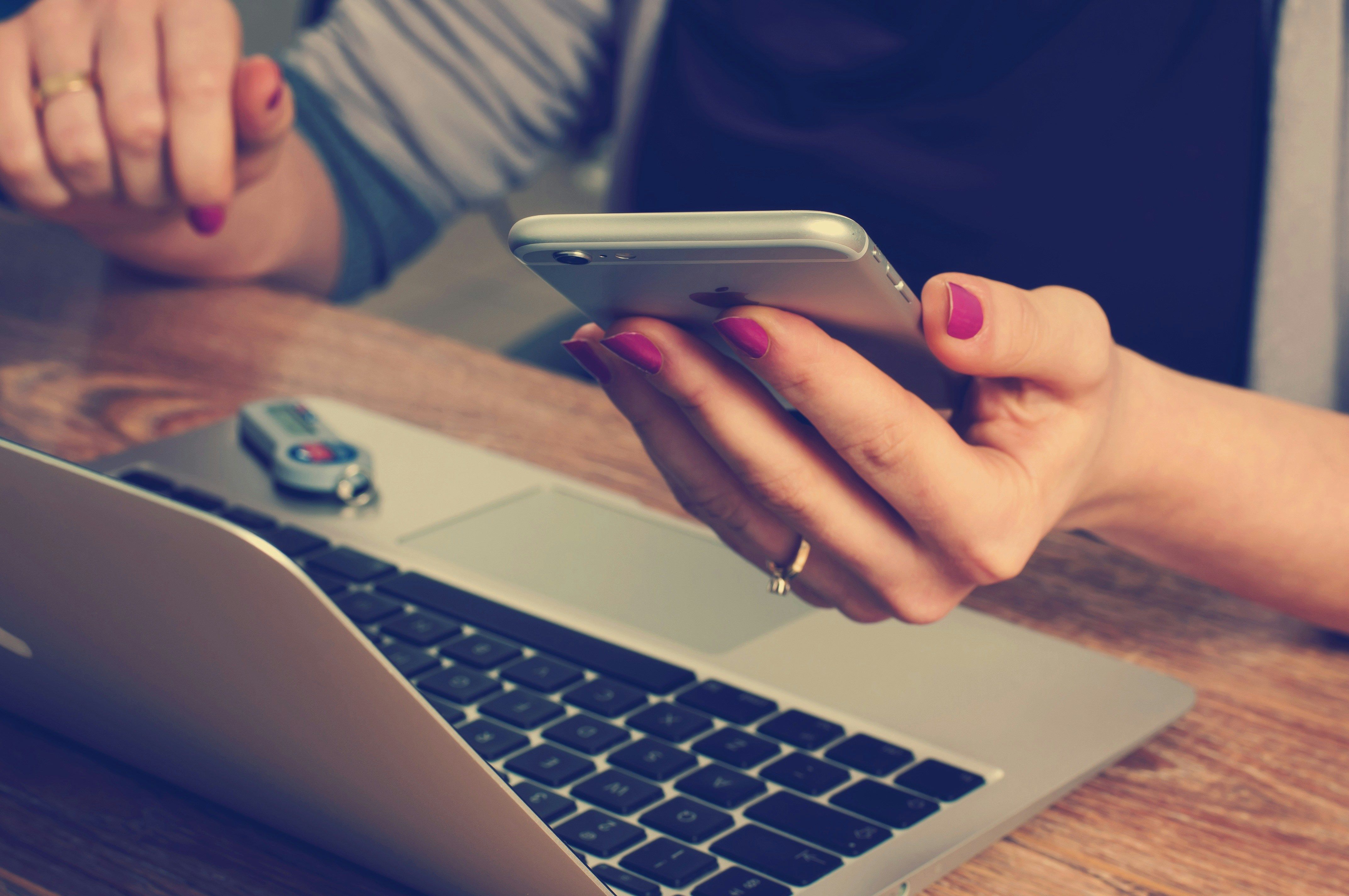 Woman looking at a phone while using a laptop 
